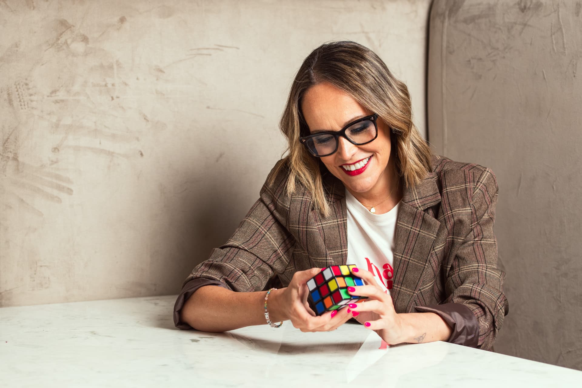 Claire Marshall seated at a marble table, smiling as she turns a Rubik's cube in her hands